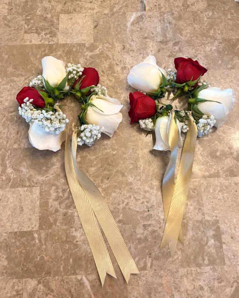 Pair of handmade floral bracelets with red and white roses, baby's breath, and gold ribbon